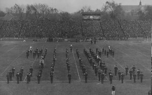 the band stands in an I formation with bleachers filled behind them