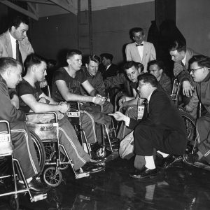 Men's wheelchair basketball team huddled around Dr. Nugent