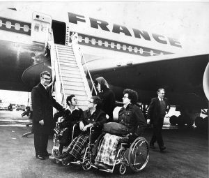 3 students in wheelchairs and Tim Nugent next to an airplane that has France on the side