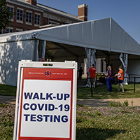 Sandwich board sign that says Walk Up Covid-19 Testing in front of a white tent