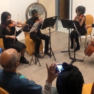 3 string musicians playing with 2 audience members visible