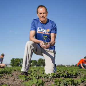 Stephen Long kneeling in a field holding a small plant