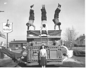 3 people do handstands on top of a bus, two people hang off the side and one person is in the middle.
